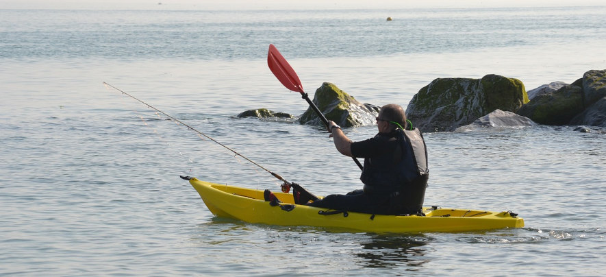 Gul fiskekajak, man paddlar med fiskespö framför sig