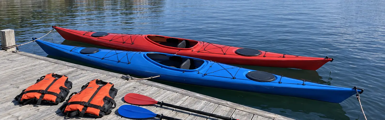Röd och blå havskajak förtöjda vid en brygga i skärgården, med flytvästar och paddlar framlagda på bryggan