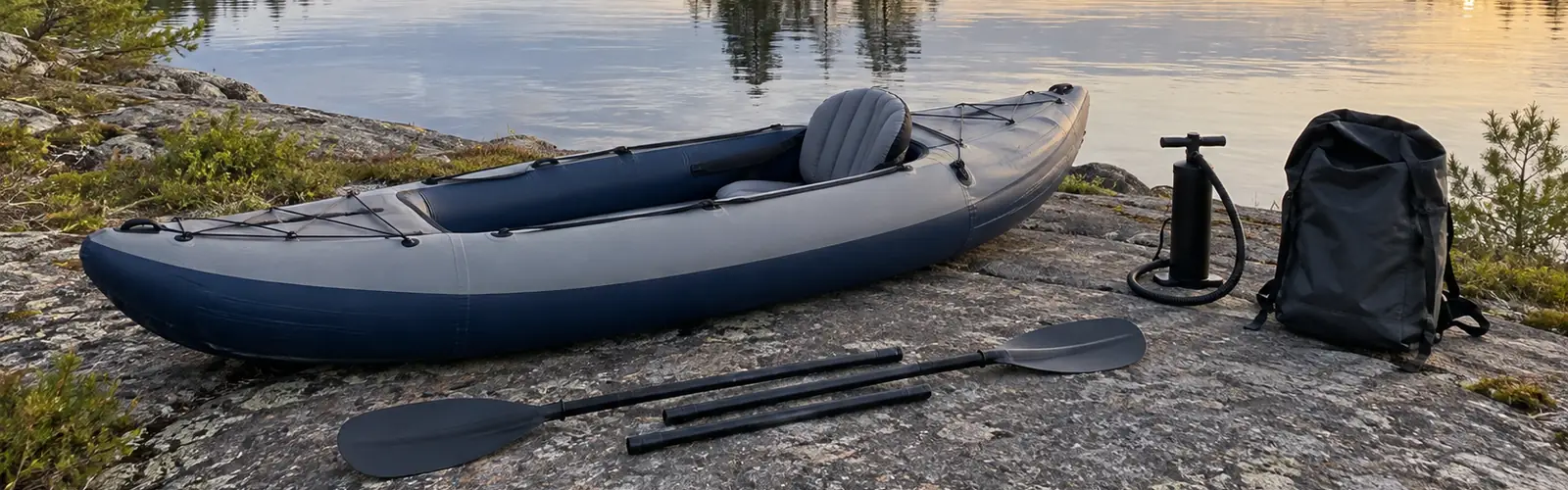 Uppblåst kajak på en klipphäll vid en sjö, med handpump, packväska och isärtagen paddel bredvid