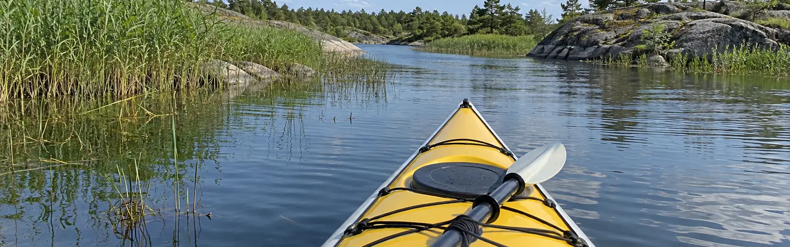 Vy från sittbrunnen över den gula fördäcket mot en slingrande kanal mellan vass och klippor