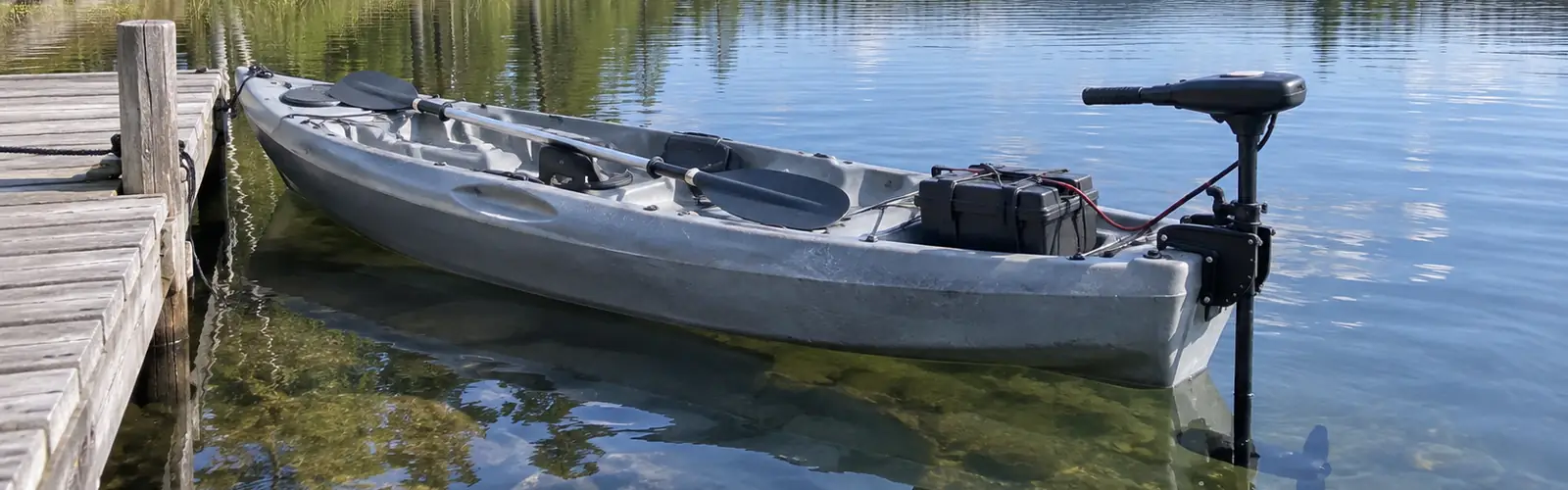 Grå sit-on-top-kajak med elmotor monterad i aktern och batterilåda, förtöjd vid en träbrygga