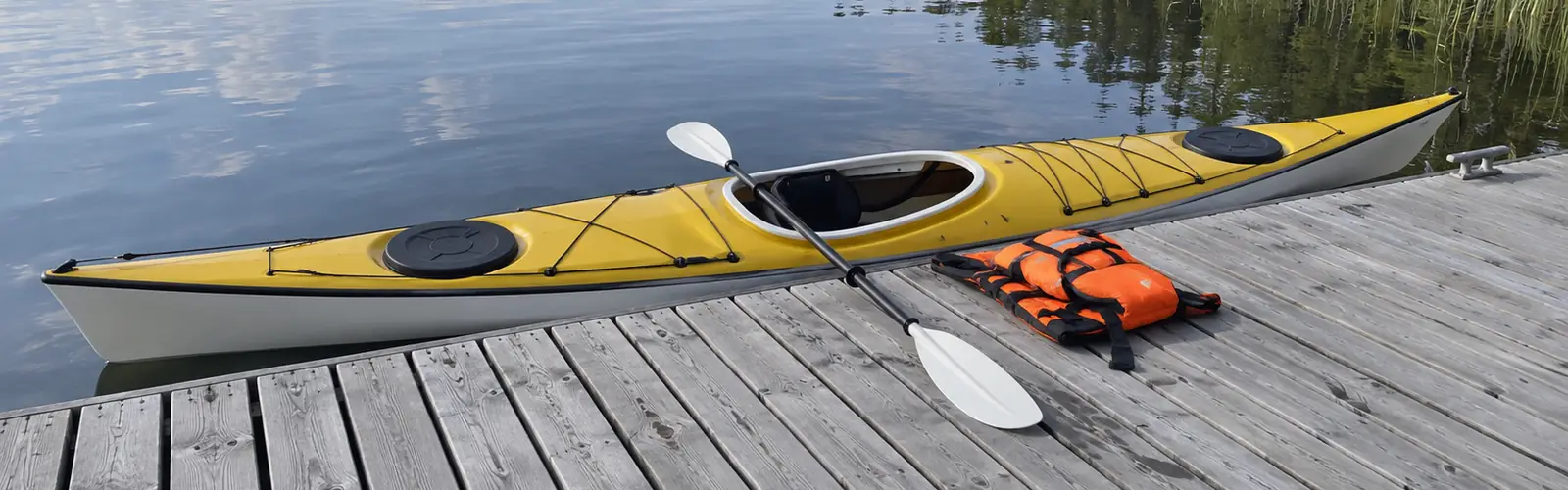 Havskajak parallellt längs en låg brygga, med paddeln lagd tvärs över kajaken och ena bladet på bryggan, och en flytväst redo