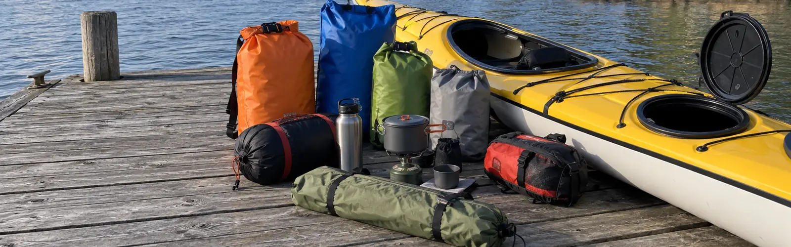 Packpåsar, tält och kök utlagda på bryggan bredvid kajaken med öppen lucka